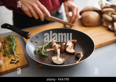 Tranches de champignons frais sont assis dans un moule sur une planche en bois, prêt à être mis sur la cuisinière. Dans l'arrière-plan, une femme plus de tranches de champignons frais. Banque D'Images