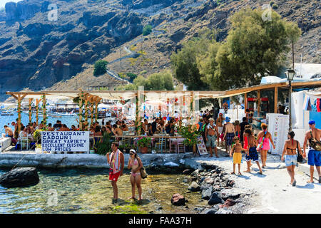 Les Cyclades, Santorin, Thirasia. Korfos, Cadouni, un café, un restaurant sur le littoral. Encombrée de touristes à manger tables et chaises. Grand panneau, bas prix. Banque D'Images