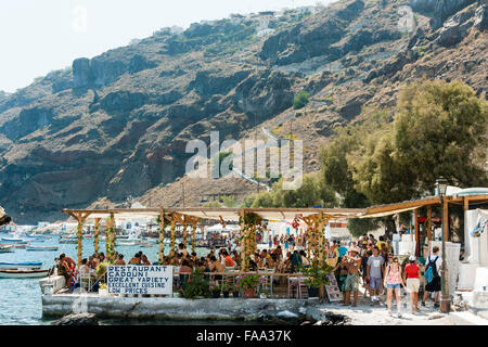 Les Cyclades, Santorin, Thirasia. Korfos, Cadouni, un café, un restaurant sur le littoral. Encombrée de touristes à manger tables et chaises. Grand panneau, bas prix. Banque D'Images