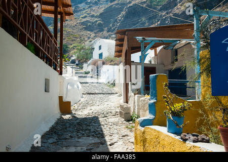 Santorin, Thirasia. Chemin d'épaulement pavées entre bâtiments rustiques menant à Manolas de Korfos Port. Deux personnes marchant vers le bas. Le jour, la lumière du soleil. Banque D'Images