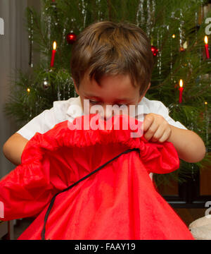 Jeune garçon opening christmas present in front of tree avec des bougies. Banque D'Images