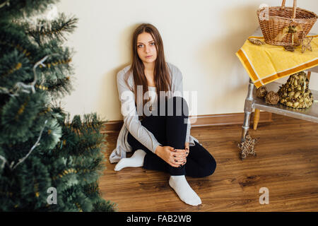 Lonely Girl sitting behind Christmas Tree with presents Banque D'Images