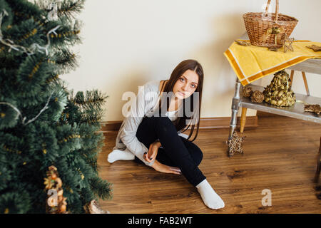 Lonely Girl sitting behind Christmas Tree with presents Banque D'Images