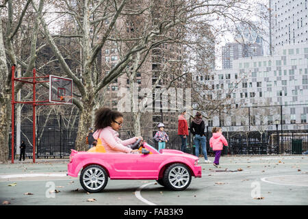 La ville de New York, vendredi, 25 décembre 2015, jour de Noël : petite fille noire avec queue touffue se concentre sur les contrôles qu'elle se rend à son tout nouveau diminutif sportscar rose sur le terrain de basket de DeWitt Clinton park dans la région de Hells Kitchen Banque D'Images