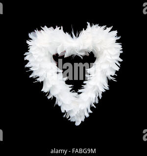 Les plumes blanches disposées en forme de coeur isolé sur noir. Banque D'Images