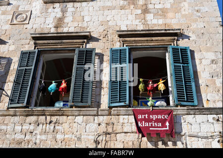 Les petites marionnettes suspendu à une chaîne en dehors de deux fenêtres avec volets en bois, Dubrovnik, Croatie. Banque D'Images