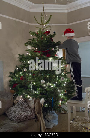 Un garçon décore l'arbre de Noël avec un chapeau sur Banque D'Images