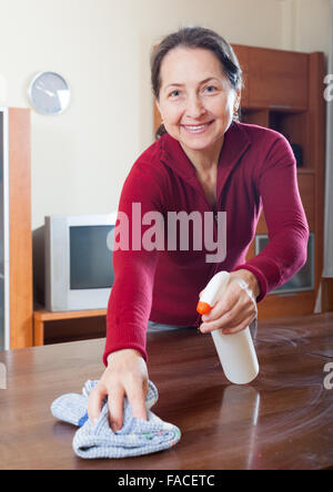 Mature Woman dusting table en bois, chiffon nettoyant et à la maison Banque D'Images