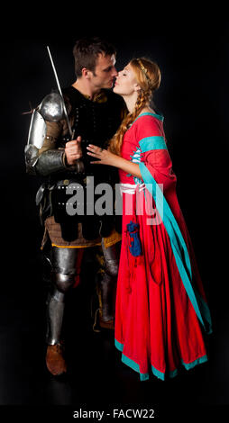 Studio shot of young couple habillé en chevalier médiéval et les baisers de jeune fille sur fond noir Banque D'Images