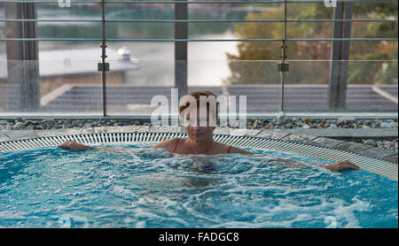 Middle aged woman relaxing in jacuzzi avec grande fenêtre Banque D'Images