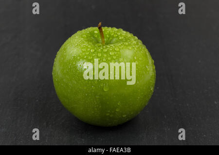 Gros plan d'une pomme verte entier frais, couvert de gouttelettes d'eau, avec pierre sous ardoise naturelle. Selective focus on fron Banque D'Images