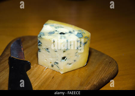 Close up d'un morceau de fromage bleu et je couteau sur une plaque de bois sur une table Banque D'Images