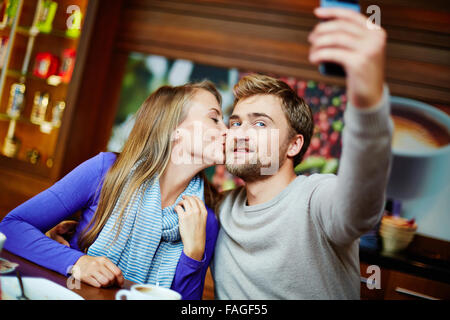 Ce jeune homme tandis que sa femme selfies embrasser in cafe Banque D'Images