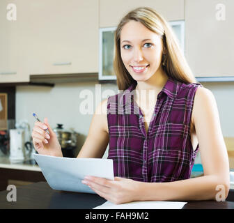 Happy blonde femme avec des papiers à la maison cuisine Banque D'Images