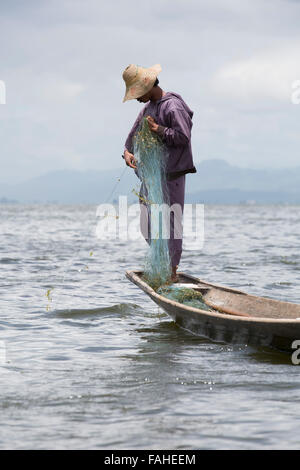 Un pêcheur de l'ethnie Intha rassemble son peuple net sur le lac Inle au Myanmar (Birmanie). L'homme est l'un des rameurs de la jambe, qui peut row Banque D'Images