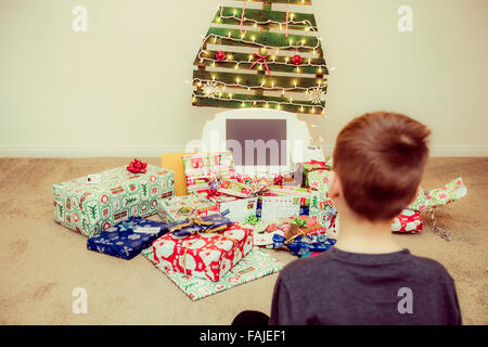 Jeune garçon regarde les cadeaux de Noël sous un arbre de Noël réutilisable, écologique Banque D'Images