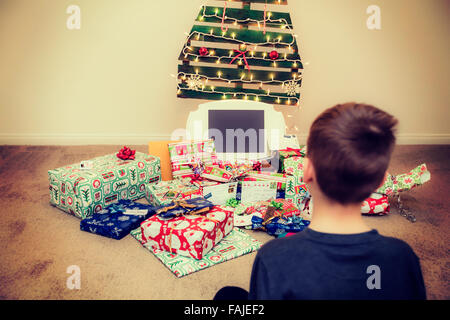 Jeune garçon regarde les cadeaux de Noël sous un arbre de Noël réutilisable, écologique Banque D'Images