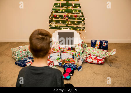 Jeune garçon regarde les cadeaux de Noël sous un arbre de Noël réutilisable, écologique Banque D'Images