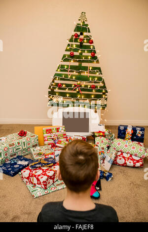 Jeune garçon regarde les cadeaux de Noël sous un arbre de Noël réutilisable, écologique Banque D'Images