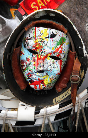 Un seul masque de carnaval de Bâle montrant un visage souriant coloré et lumineux dans un vieux casque de l'armée qui met sur une caisse claire. Banque D'Images