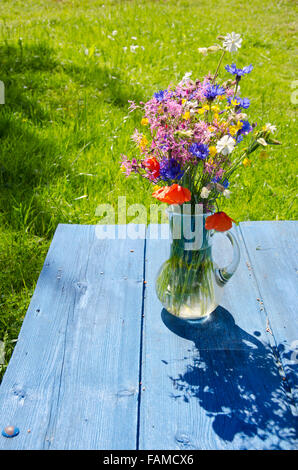 Fleurs sauvages dans un pot sur la table bleu par le pré vert en été aux beaux jours Banque D'Images