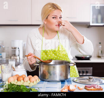 Jeune femme prend couvercle de casserole et sentir le renfermé à la maison cuisine Banque D'Images