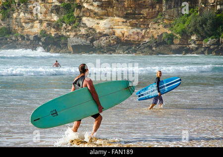 Un homme et une femme surfeur quittent l'eau lors d'une matinée ensoleillée à Freshwater Beach en Australie Banque D'Images