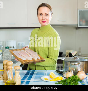 Cheerful woman avec tranches de poisson près du point d'ébullition pan au cuisine Banque D'Images