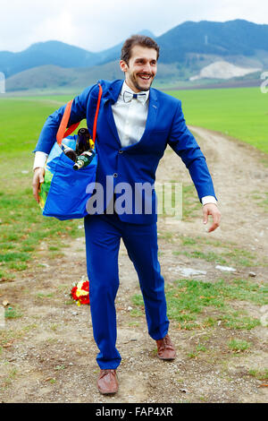 Jeune beau palefrenier en costume bleu avec un sac rempli de bouteilles de bière Banque D'Images