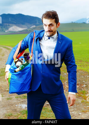 Jeune beau palefrenier en costume bleu avec un sac rempli de bouteilles de bière Banque D'Images