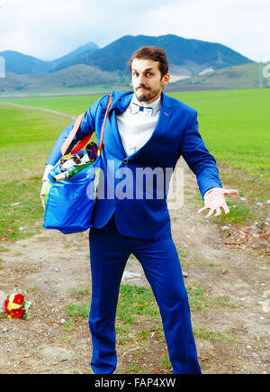 Jeune beau palefrenier en costume bleu avec un sac rempli de bouteilles de bière Banque D'Images