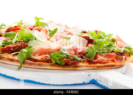 Pizza culinaire avec prosciutto, tomates et fines herbes sèches sur planche à découper en bois sur tableau blanc. Banque D'Images