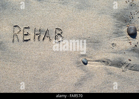 Le mot REHAB écrit dans le sable. Banque D'Images