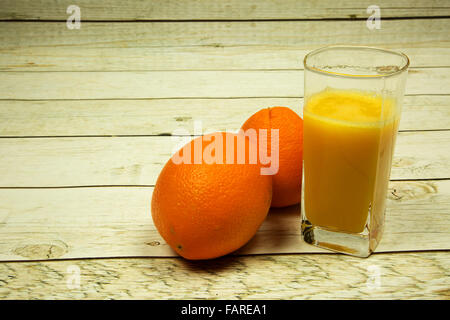 Un verre de jus et deux oranges sur un sol en bois, vieux, comptoir en vert style vintage. Vue horizontale. Banque D'Images