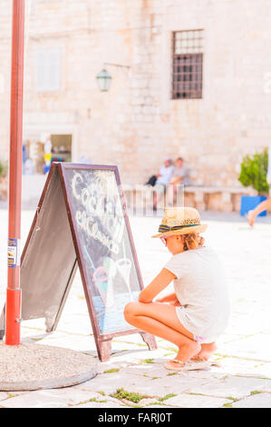 Petite fille en vacances lit le tableau à l'extérieur d'un restaurant bar dans l'île de Hvar, Croatie, Europe. Banque D'Images