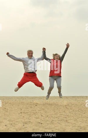 Mature couple jumping on beach Banque D'Images