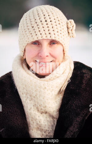 Un hiver portrait of a smiling senior femme portant un chapeau de laine et une écharpe, avec un fond de neige Banque D'Images