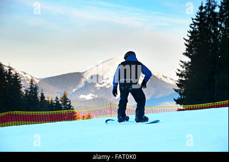 Snowboarder méconnaissable sur une pente de montagne au coucher du soleil en action Banque D'Images