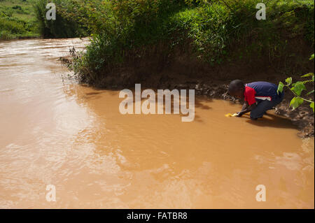 Jeune garçon obtenir de l'eau d'une rivière boueuse pour une utilisation comme eau de boisson. Au Kenya. Banque D'Images