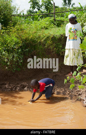 Jeune garçon obtenir de l'eau d'une rivière boueuse pour une utilisation comme eau de boisson. Au Kenya. Banque D'Images