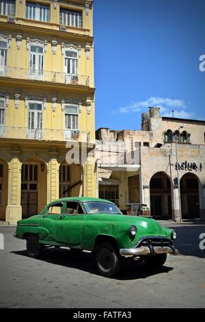 Beat up old vintage verte voiture garée dans un square ensoleillé dans la Vieille Havane, Cuba, entouré de bâtiments de style colonial Banque D'Images