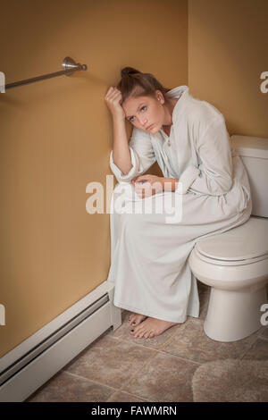 Teenage girl sitting dans la salle de bains sur le siège des toilettes à la malheureuse Banque D'Images