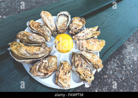 Une douzaine d'huîtres et un citron sur une plaque en plastique de manger à l'extérieur près de la mer Banque D'Images