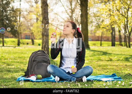 Rêve de désirs. Belle jeune étudiante fille assise sur un pré, soufflant des bulles de savon, faire une pause à partir de l'étude. Banque D'Images