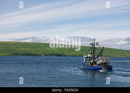 Un bateau de pêche transportant une yole motors hors de Sand Point Harbor, sud-ouest de l'Alaska, USA, l'été Banque D'Images