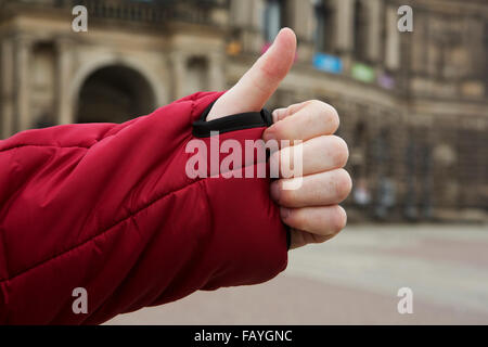 Un homme fait un Thumbs up geste. Son pouce se moque à travers le poignet d'une boucle veste rouge. Banque D'Images