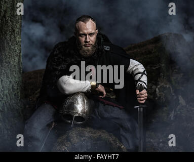 À l'épée et le casque de Viking sur fond de forêt de fumée. Repos du Guerrier. Costume historique. Banque D'Images