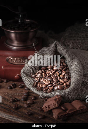 Sac de grains de café sur un fond sombre. Moulin à café vintage et de morceaux de chocolat sur une table en bois. Banque D'Images