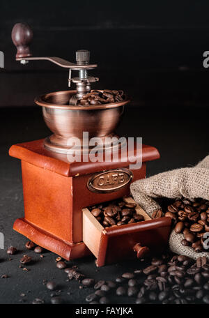 Grains de café dans des sacs de jute avec broyeur de café sur fond de bois sombre. Banque D'Images