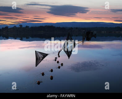 Coucher de soleil sur le lac avec des filets de poisson dans des bleus, des jaunes et rose et teintée de rose les nuages reflètent dans l'eau Banque D'Images